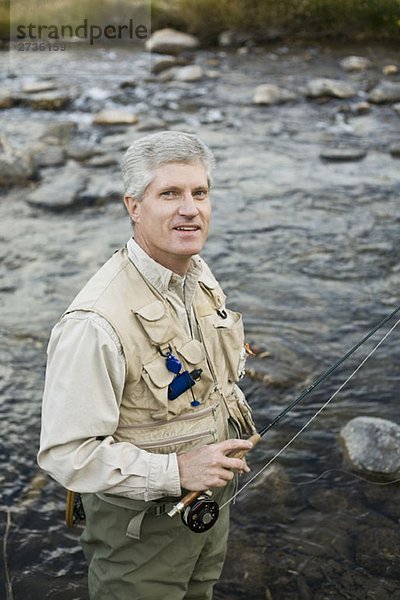 Ein Mann  der in einem Fluss steht und eine Fliegenrute hält.