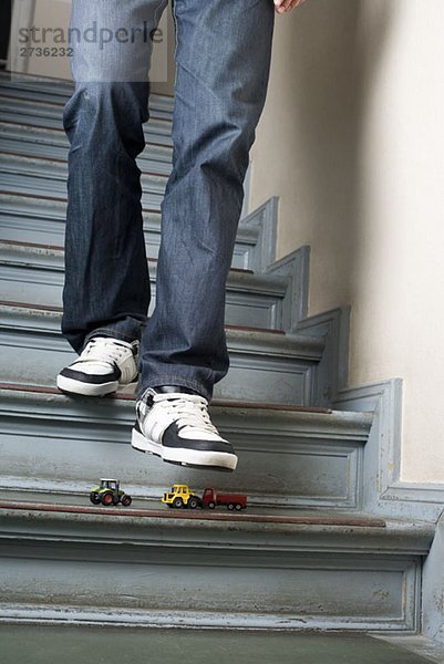 Ein Mann  der die Treppe hinuntergeht  um auf Spielzeugautos zu treten.