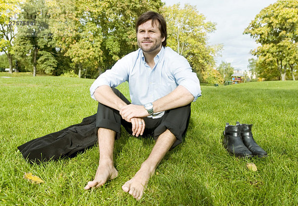 Mann sitzt barfuß auf dem Rasen