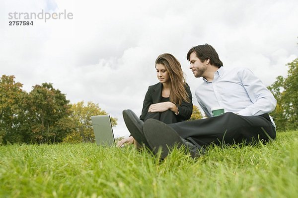 Frau und Mann auf dem Rasen sitzend mit Computer