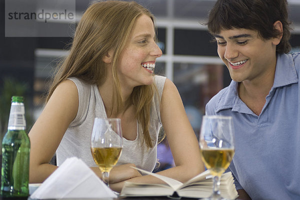Junges Paar sitzt in einem Café im Freien und schaut sich gemeinsam das Buch an.