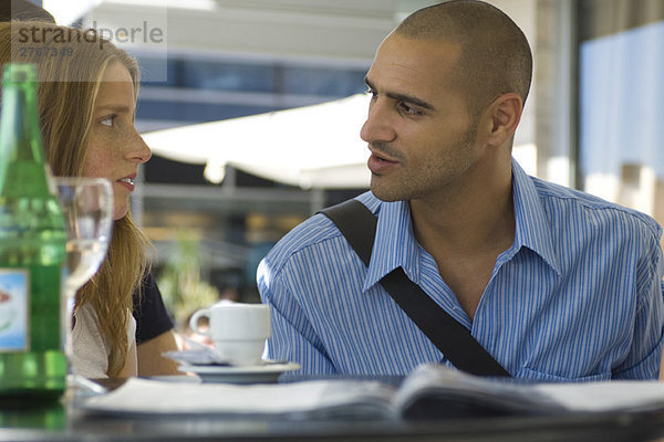 Mann und Frau sitzen in einem Café im Freien und unterhalten sich ernsthaft.