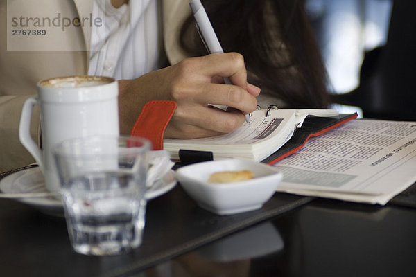 Frau sitzt im Cafe  schreibt in der Agenda  Ausschnittansicht