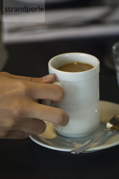 Frauenhand hebt Tasse Kaffee auf  Nahaufnahme