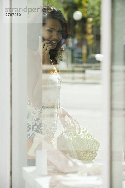 Frau schaut ins Schaufenster  spricht mit dem Handy