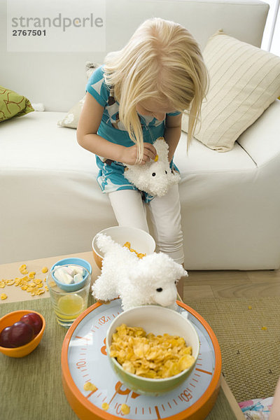 Kleines Mädchen füttert Müsli an ausgestopftes Spielzeug