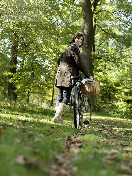 Reife Frau zu Fuß mit Fahrrad im park