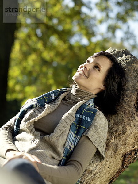 Reife Frau auf abgefallener Baum sitzen und lächelnd