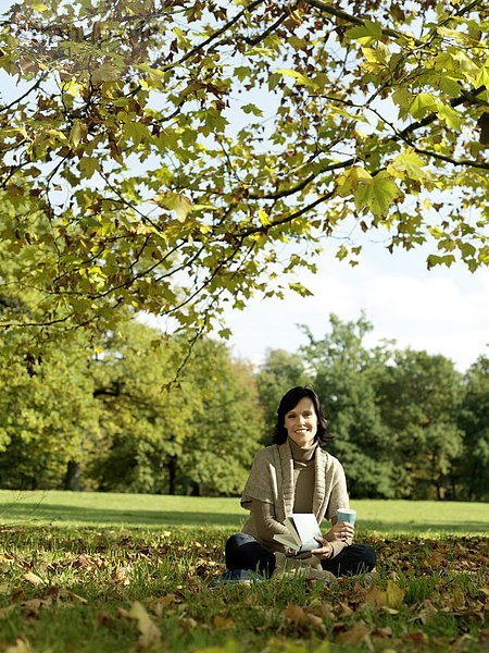 Portrait reife Frau hält Buch und lächelnd im park