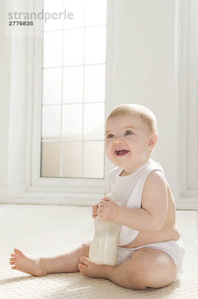 Ein Baby sitzt und hält eine Milchflasche.