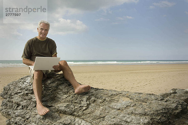 Ein Mann am Strand  der seinen Computer benutzt.