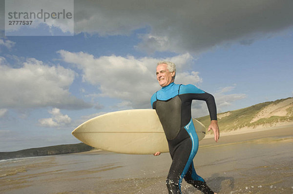 Ein Mann  der mit einem Surfbrett ins Meer läuft.