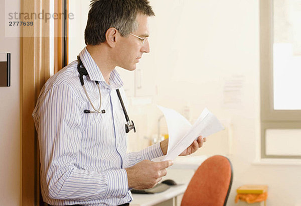 Ein männlicher Arzt  der sich einige Papiere ansieht.