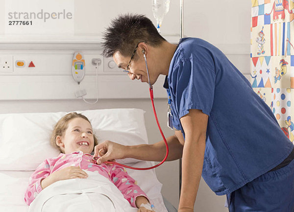 Ein männlicher Arzt hört auf das Herz eines Mädchens.