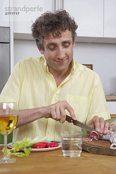 Mann zu Hause beim Schneiden von Salami