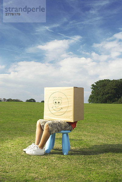 Junge auf Hocker mit Box auf Kopf