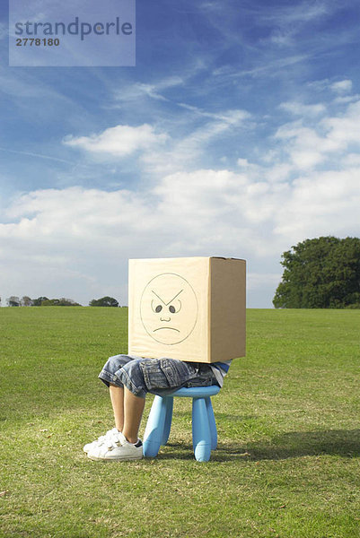 Junge auf Hocker mit Box auf Kopf