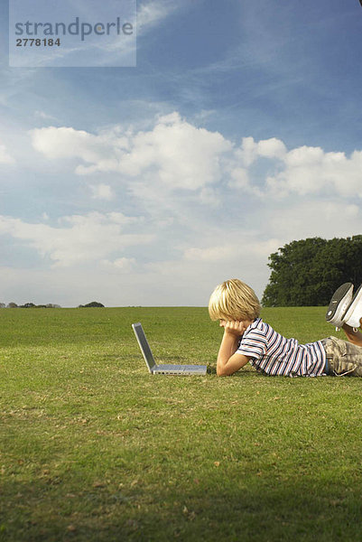 Junge schaut auf Laptop im Feld