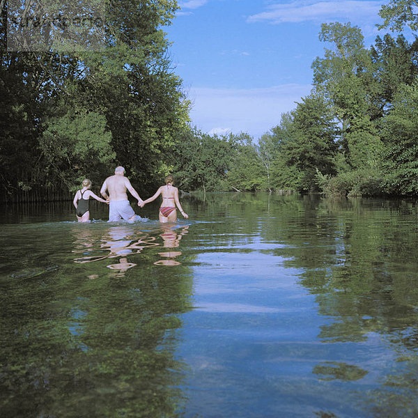 Mann und zwei Mädchen waten im Fluss