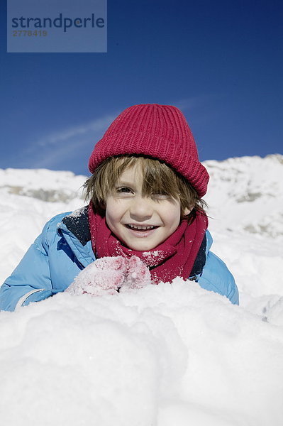 Portrait eines jungen auf Schnee liegen und lächelnd