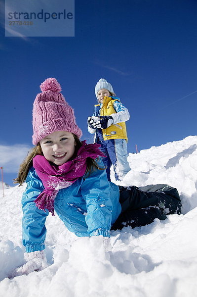 Porträt des Mädchens auf Schnee liegen und lächelnd mit jungen im Hintergrund