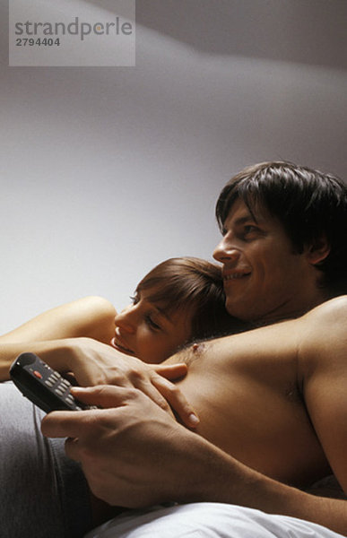 Junges Paar  zusammen im Bett liegend  fernsehend  lächelnd
