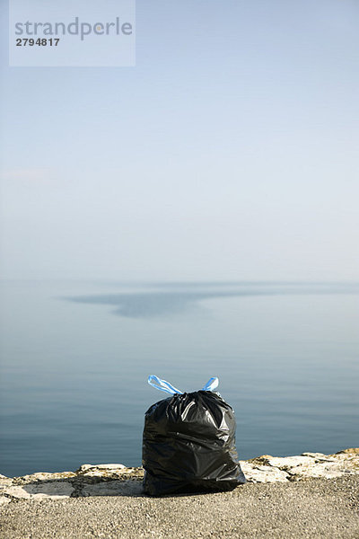 Müllsack auf Felsvorsprung mit Meer im Hintergrund