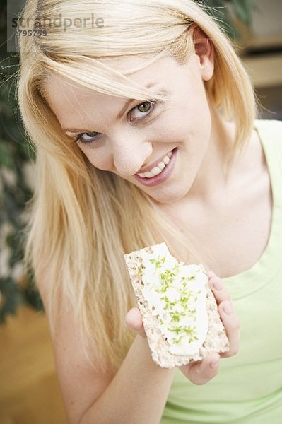 Junge Frau isst Knäckebrot mit Quark und Kresse