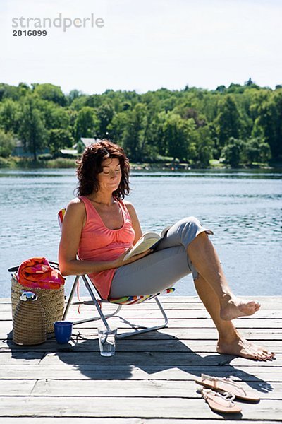 Eine Frau  lesen ein Buch über eine Mole ein See Schwedens.