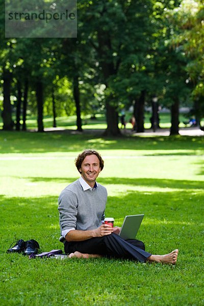 Ein Mann mit einem Laptop in einem Park Schweden.