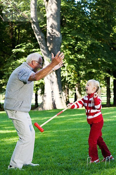 Mädchen und älterer Mann spielen Krocket im Park Schweden.