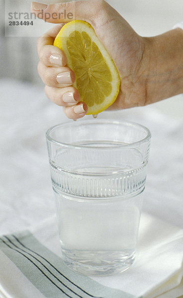 Hand Sqeezing eine Zitrone in ein Glas