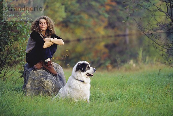 27 Jahre alte hellhäutige Frau sitzend auf einem Felsen mit einem großen Pyranee Hund während der Herbst-Saison  Saint Calixte  Québec  Kanada.