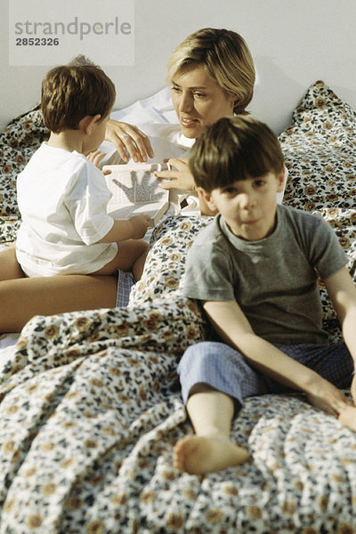 Mutter und zwei Kinder  die im Bett faulenzen.