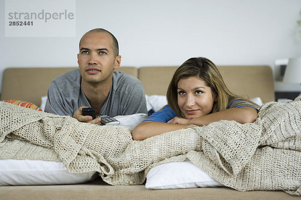 Paar liegt auf dem Bett und schaut gemeinsam fern.