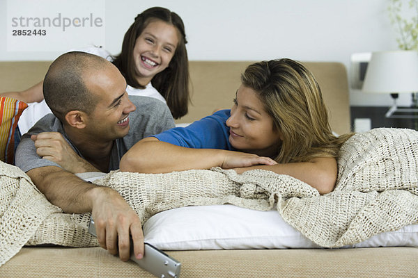Familie entspannt sich gemeinsam auf dem Bett  Mann und Frau lächeln sich an.