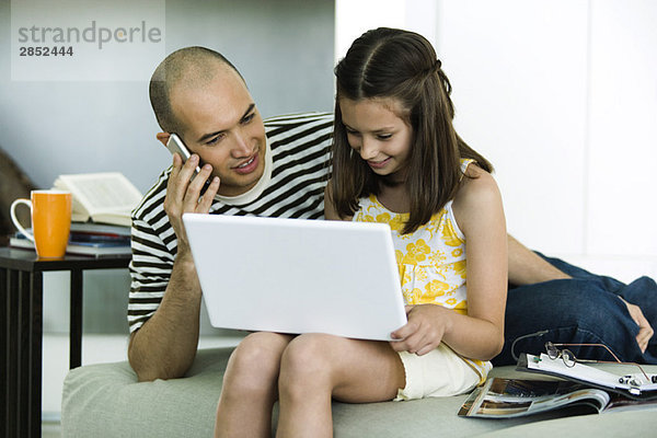 Vater und Tochter schauen zusammen auf Laptop-Computer  Mann mit Handy