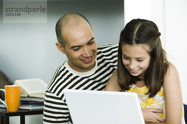 Vater und Tochter benutzen gemeinsam einen Laptop-Computer
