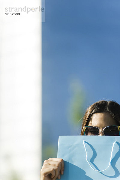 Junge Frau mit Sonnenbrille und Einkaufstasche vor dem Gesicht