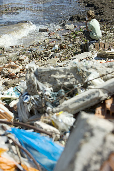 Junge kauert auf verschmutztem Ufer  trägt Verschmutzungsmaske