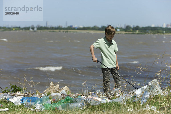Junge sammelt Müll an verschmutztem Ufer auf