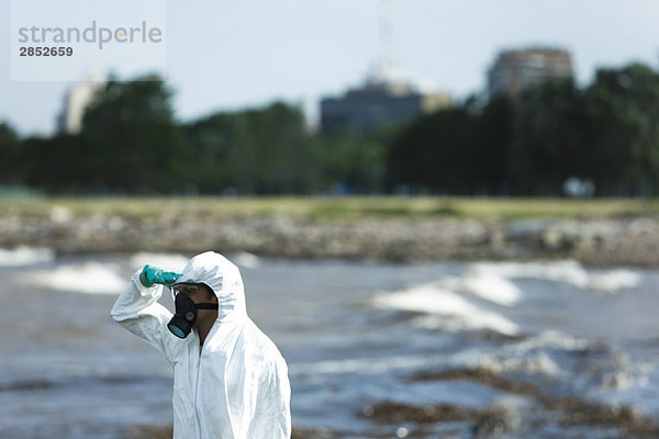 Person im Schutzanzug mit Blick auf verschmutztes Wasser  Seitenansicht