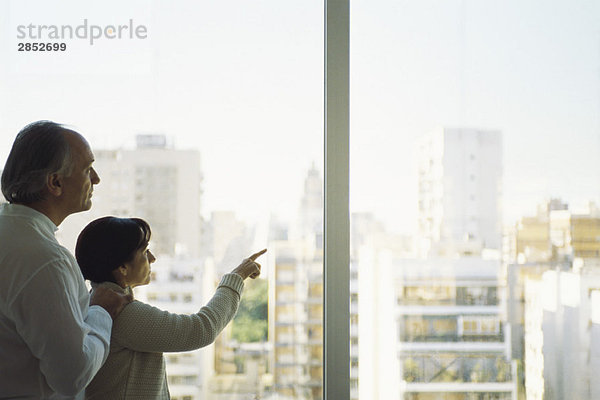 Ein reifes Paar am Fenster mit Blick auf die Skyline der Stadt  Frau  die darauf zeigt