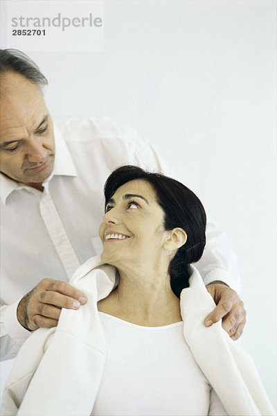 Mann legt Jacke um die Schultern seiner Frau  Frau sieht ihn lächelnd an.