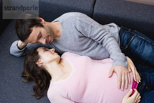Schwangere Frau und Mann auf der Couch liegend