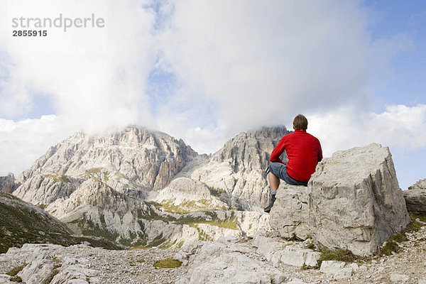 Mann sitzt auf Felsen und schaut auf Gipfel