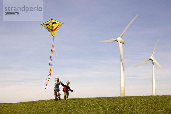 Zwei Jungen fliegender Drachen an Windkraftanlagen