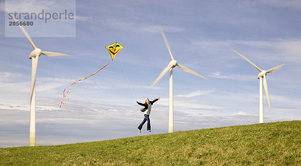 Mann springt mit Drachen an Windkraftanlagen