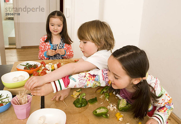 Zwei Mädchen und ein Junge kochen Gemüse