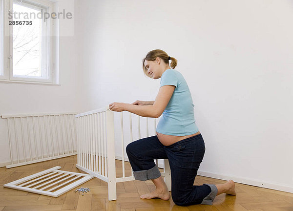 Schwangere Frau beim Zusammenstellen des Babybettes